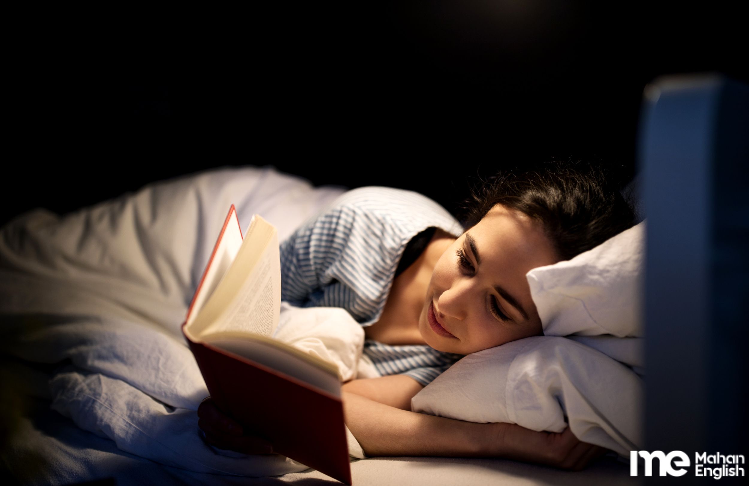 دختری زیبا در تخت خواب خود و در حال مطالعه کتاب قبل از خواب